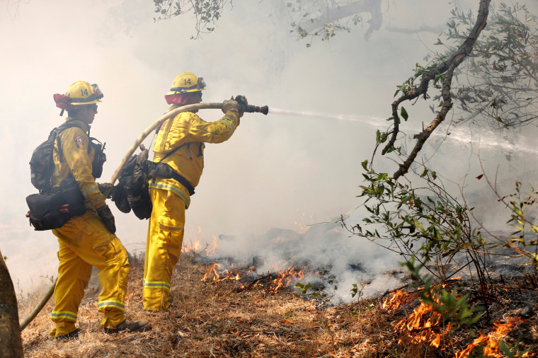 Image: CalFire firefighters spray water on a controlled back fire while battling the the so-called \"Sherpa Fire\", which has grown to over 1100 acres overnight, in the hills near Goleta
