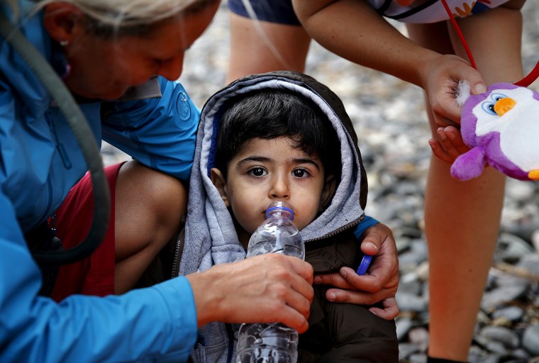 Image: Volunteers give water and toys to an exhausted Syrian refugee child soon after he and his family arrived on the Greek island of Lesbos