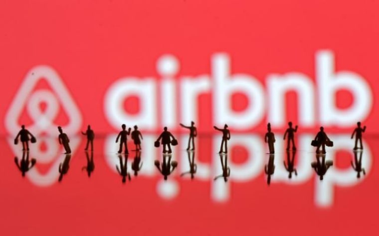 A 3D printed people's models are seen in front of a displayed Airbnb logo in this illustration