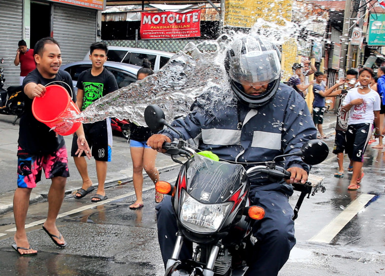 Image: A man throws a bucket of water at a motorcyclist as residents join in a water-splashing frenzy to honor their patron St. John the Baptist's Feast Day in San Juan