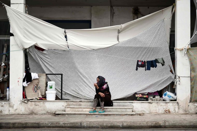 Image: A woman sits next to the makeshift tents at the unofficial camp for migrants in Athens