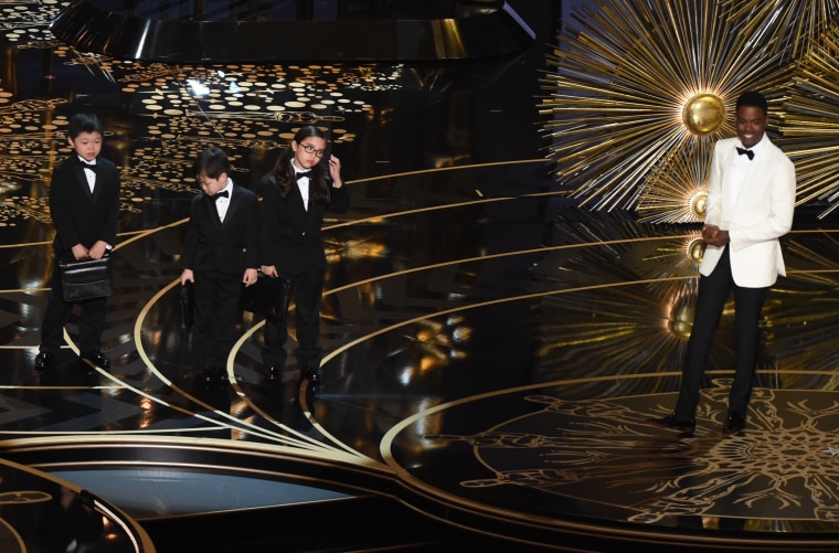 Chris Rock and three children representing accountants at the 88th Academy Awards.