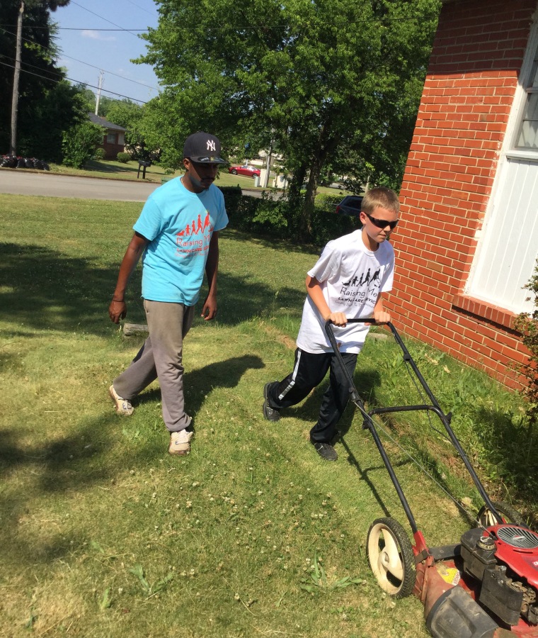 Rodney Smith, Jr., helps a young volunteer with Raising Men Lawn Care.