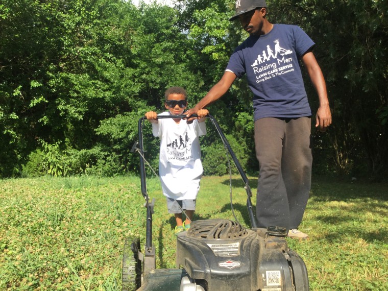 Image: Rodney Smith, Jr., helps a young volunteer with Raising Men Lawn Care give back to his community