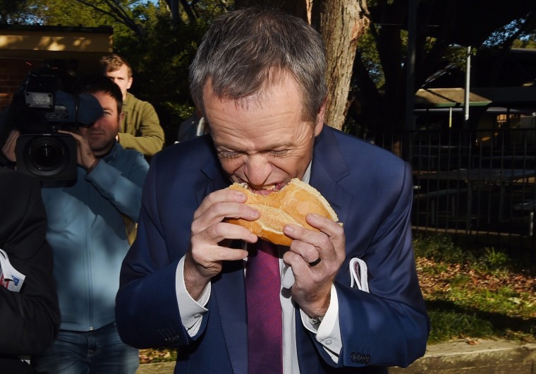 Image: Opposition leader Bill Shorten eats a sausage sandwich - controversially starting from the middle - as part of the 2016 Election Day in Sydney, New South Wales.