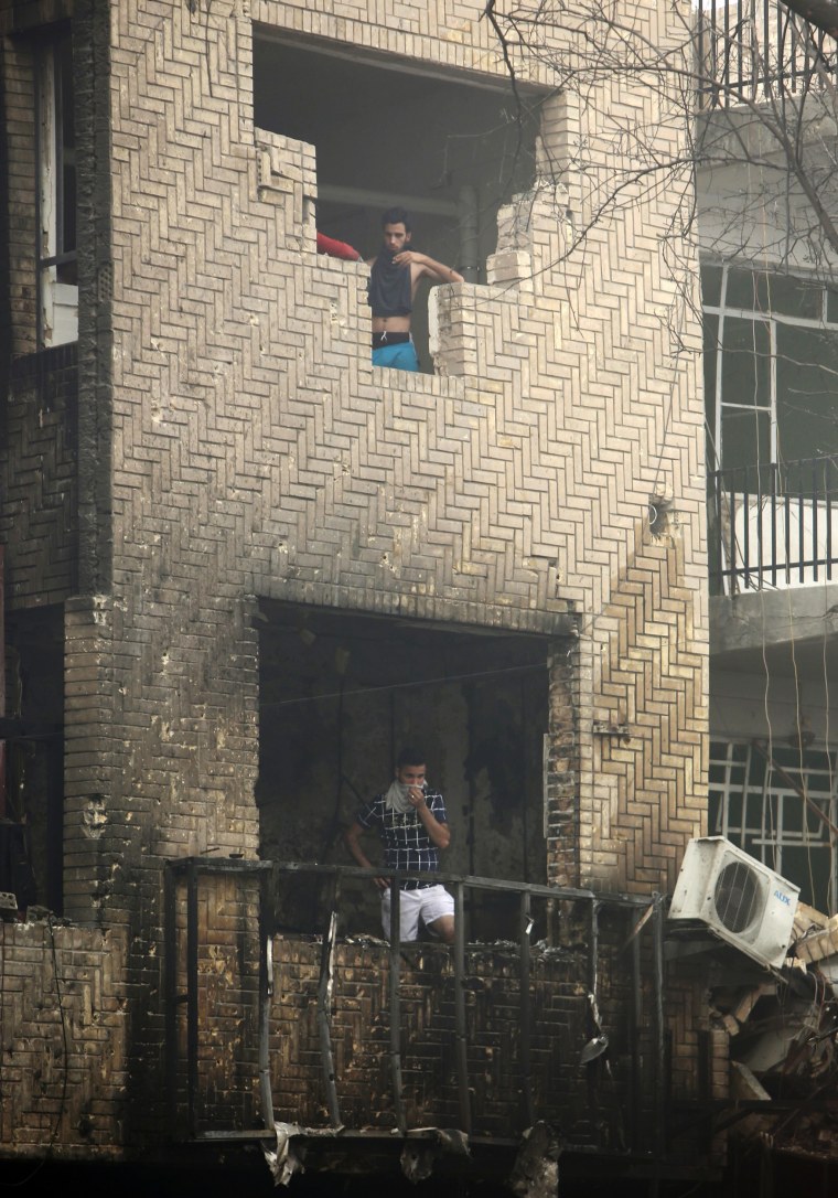 Image: Iraqi men stand inside a damaged building at the site of a suicide car bombing