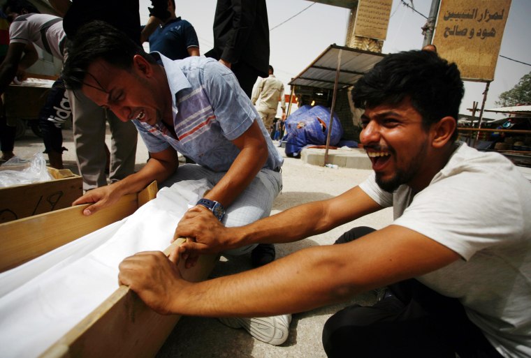 Image: Iraqi men mourn over a body after they lost five members of their family in a suicide bombing