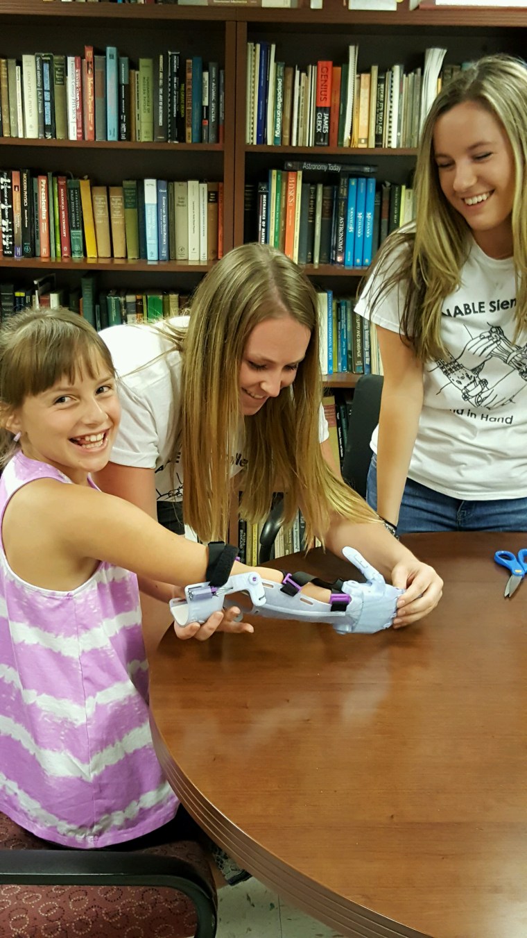 Miranda Marnes, a senior from Plattsburgh, New York, helps Karissa Mitchell put on her new arm. Alyx Gleason, an e-NABLE team leader, looks on.