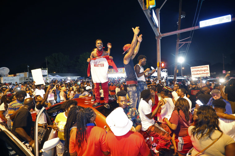 Image: Protestors stand on cars as they congregate in Baton Rouge
