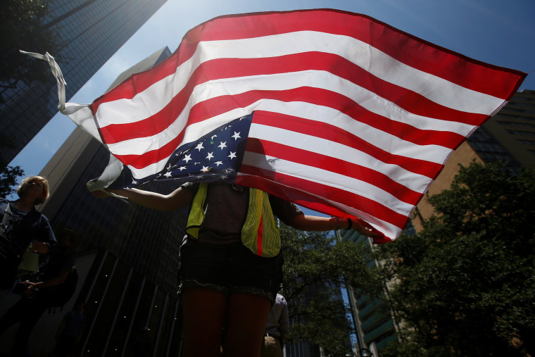 Image: A woman holds a U.S. flag during a prayer vigil in a park following the multiple police shooting in Dallas