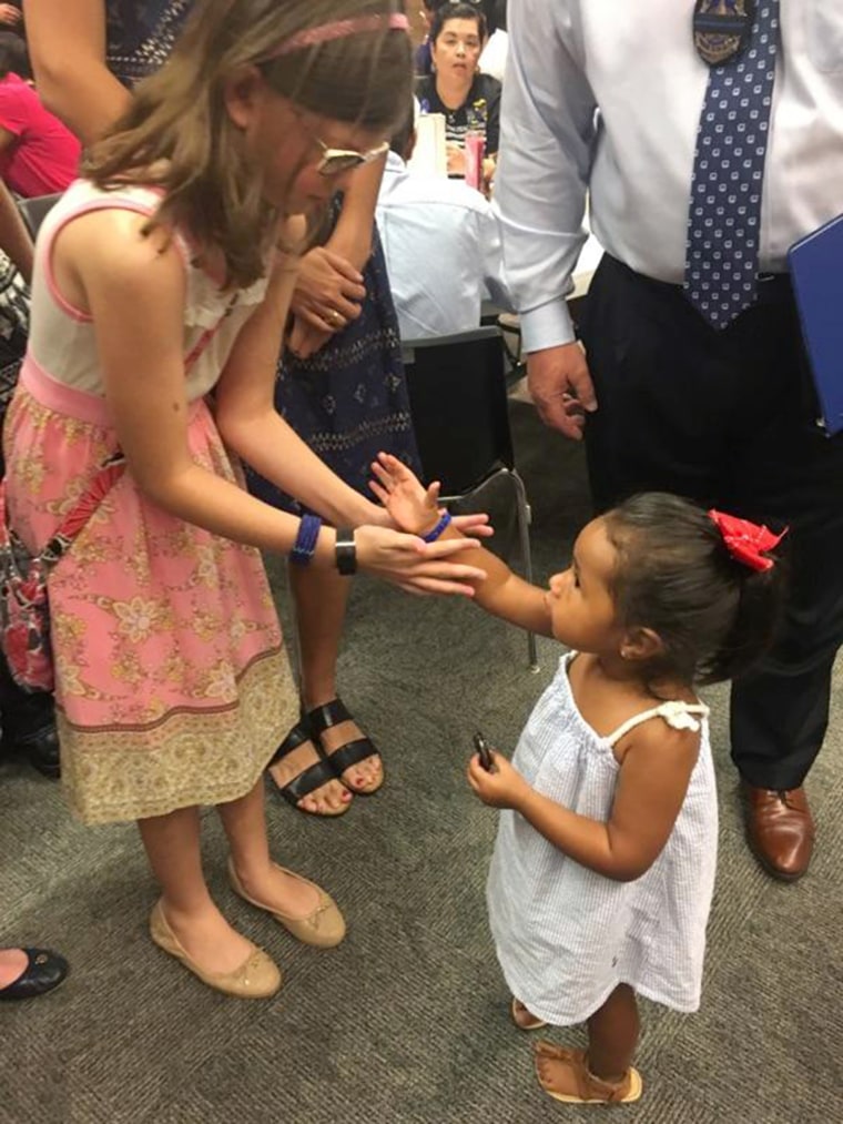 A daughter of one of the officers killed in the Dallas attack giving a bracelet to the 2-year-old daughter of another policeman who was killed during a memorial ceremony