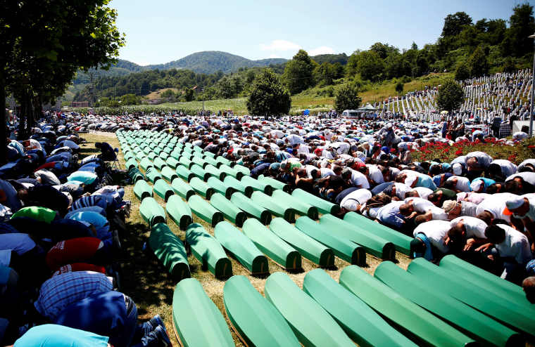 Image: Muslim men pray in front of coffins during mass funeral in Potocari near Srebrenica
