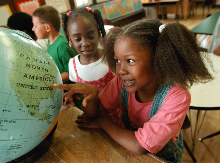 Two Black students examine globe in class.