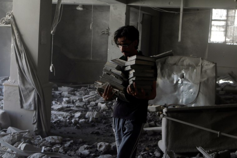 Image: A man carries Koran books he collected amid damage inside al-Aqsa mosque after an airstrike on the rebel held Al-Hilwaniyeh neighbourhood in Aleppo, Syria