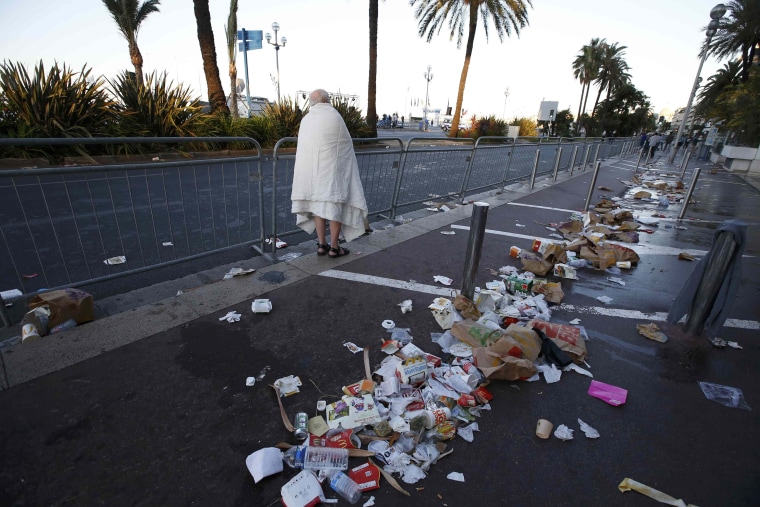 Image: A man walks through debris on the street the day after a truck ran into a crowd at high speed killing scores celebrating the Bastille Day July 14 national holiday on the Promenade des Anglais in Nice