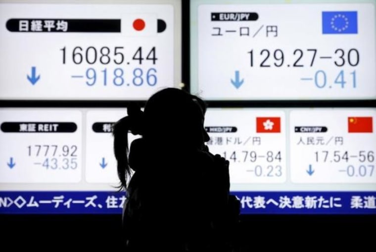 A pedestrian holding her mobile phone walks past electronic boards showing the Japan's Nikkei average and the Japanese yen's exchange rate against the euro outside a brokerage in Tokyo