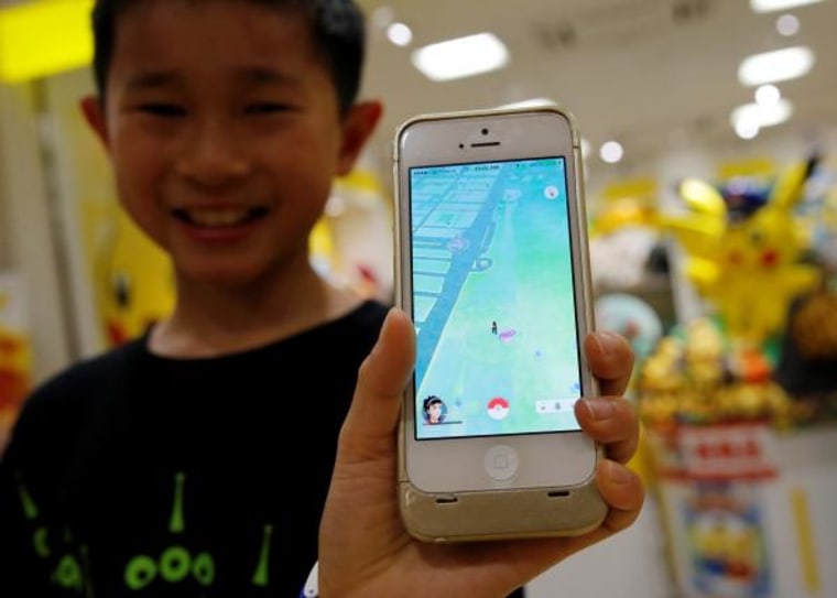 Boy poses with a mobile phone displaying the augmented reality mobile game "Pokemon Go" by Nintendoa in front of a shop selling Pokemon goods in Tokyo