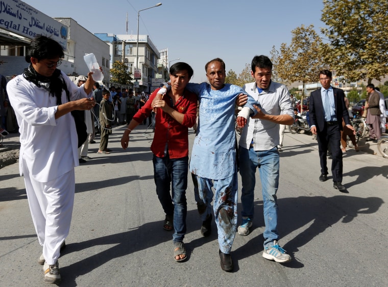 Image: Men help an injured man outside a hospital after a suicide attack in Kabul