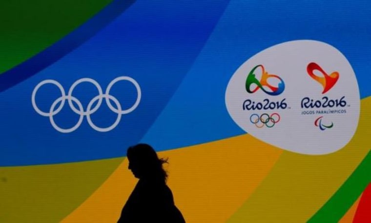 A journalist walks in front of a screen with olympics logos during the medal launching ceremony in Rio de Janeiro