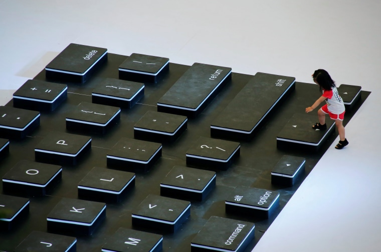 Image: A child climbs onto a giant mockup laptop keyboard during a promotion event at a shopping centre in Beijing