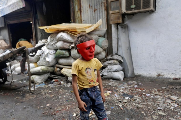 Image: A boy wearing a plastic mask walks in an industrial area in Mumbai