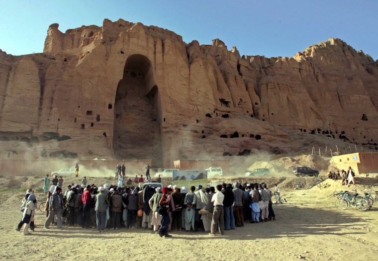 Image: Villagers stand in front of the remains of the giant Buddhas of Bamiyan