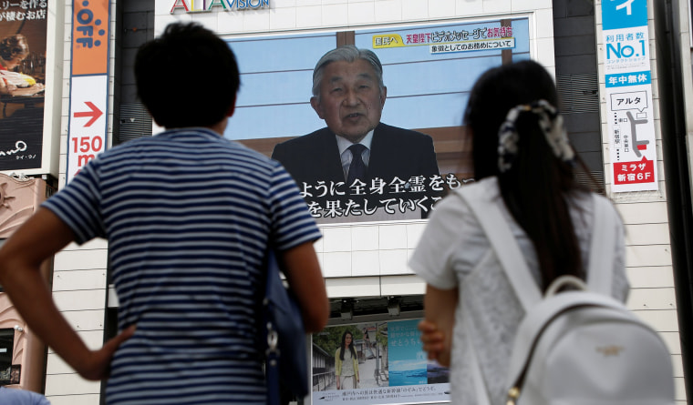 Image: People watch a large screen showing Japanese Emperor Akihito's video address in Tokyo