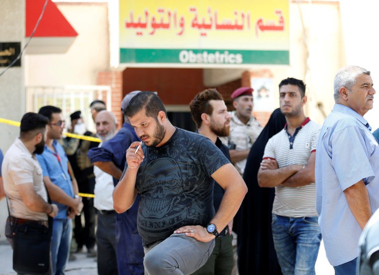 Image: People stand outside a maternity ward after a fire broke out at Yarmouk hospital in Baghdad