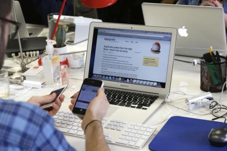 An employee uses his Iphone as he works on a computer screen displaying the AppGratis blog in the offices of AppGratis company in Paris