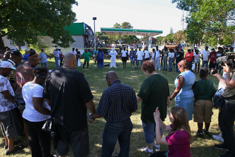 Area residents pray for peace while holding hands in a circle, next to a BP gas station burned during Saturday evening's protest in Milwaukee on Sunday, Aug. 14, 2016.