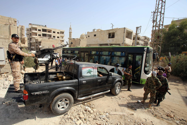 Image: Syrian government troops stand guard as a bus carrying people drives by