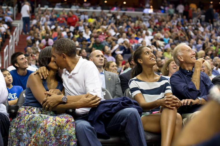 United States President, Barack Obama, and First Lady, Michelle Obama, kissing for the benefit of the kiss cam during a basketball game between the U.S. Men's Olympic basketball team and Brazil in Washington, D.C. The audience cheered as Malia Obama and the Vice President, Joe Biden, watched overhead on the Jumbotron.