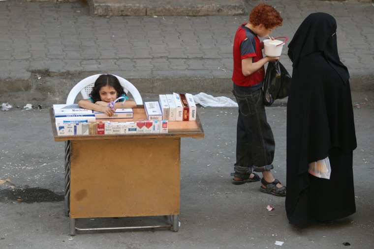 Image: A boy eats yogurt near a girl selling cigarettes in the rebel held al-Shaar neighborhood of Aleppo