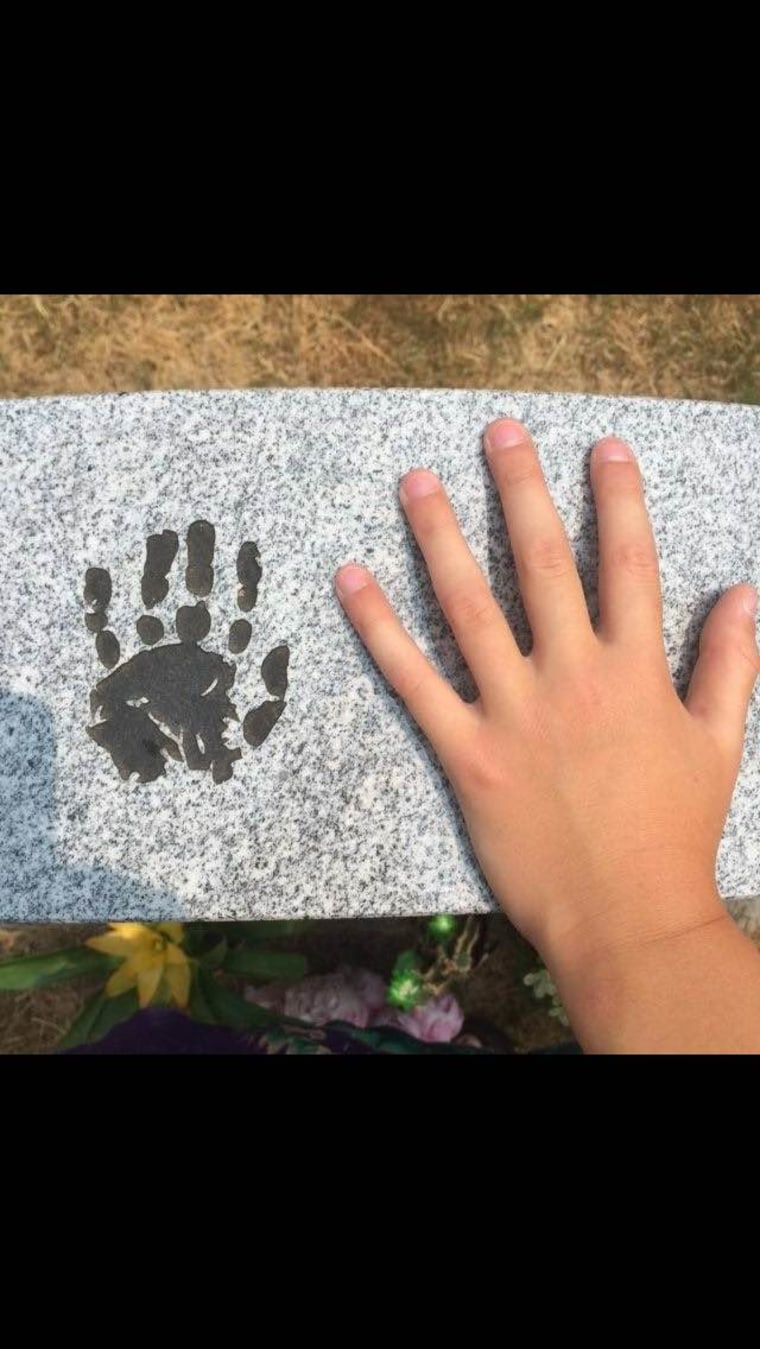 Linda's 9-year-old son places his hand next to his brother's handprint on his grave marker.