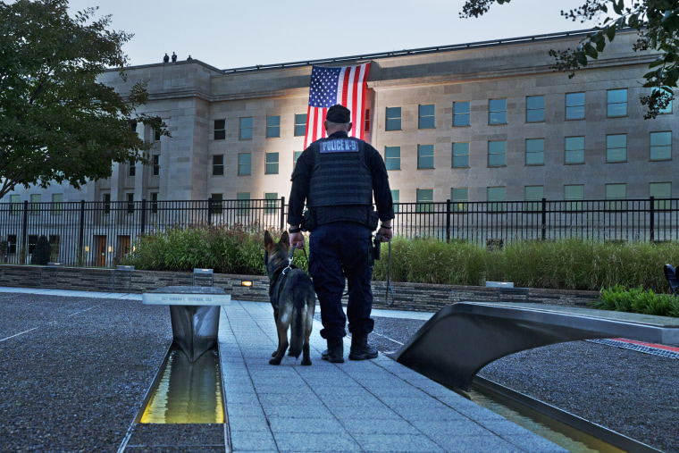 Standing at the Pentagon Memorial, a K-9 officer pauses as he looks toward the U.S. flag as it is draped on the side of the Pentagon where the building was attacked, on Sept. 11, 2015, the 14th anniversary of the attack.