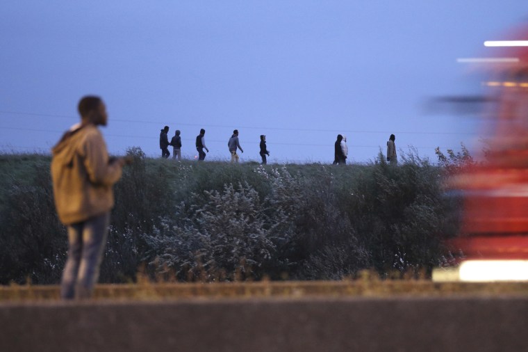 Image: Migrants walk on a ridge above a road in Calais, France