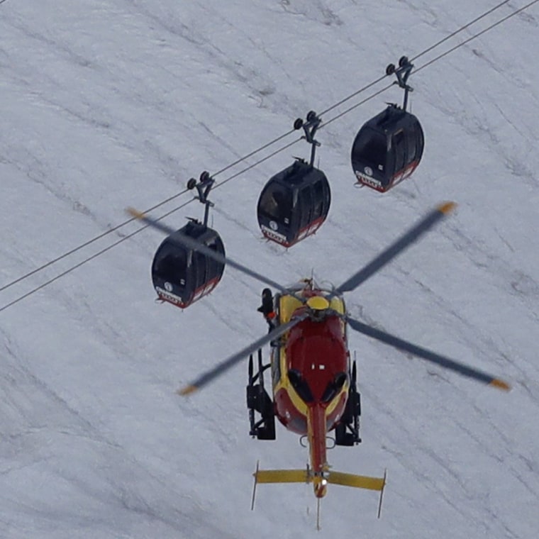 Image: An EC-135 helicopter operated by the French Societe' Civile hovers near three cars of the Panoramic Mont Blanc cable car that stalled