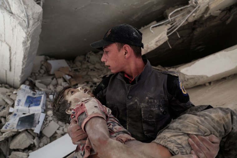 Image: A young Syrian rescue worker carries a wounded boy away from the rubble of a building in Douma, Syria