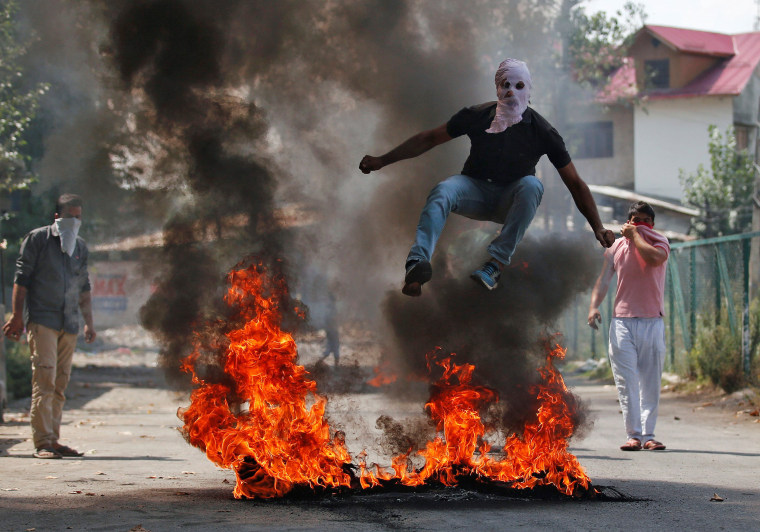 Image: A man in a balaclava jumps over burning debris during a protest against the recent killings in Kashmir, in Srinagar