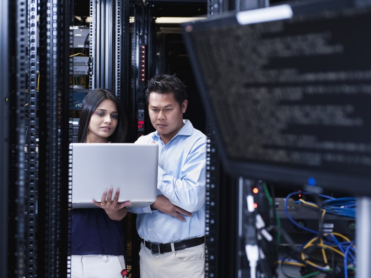 Business people using laptop in server room