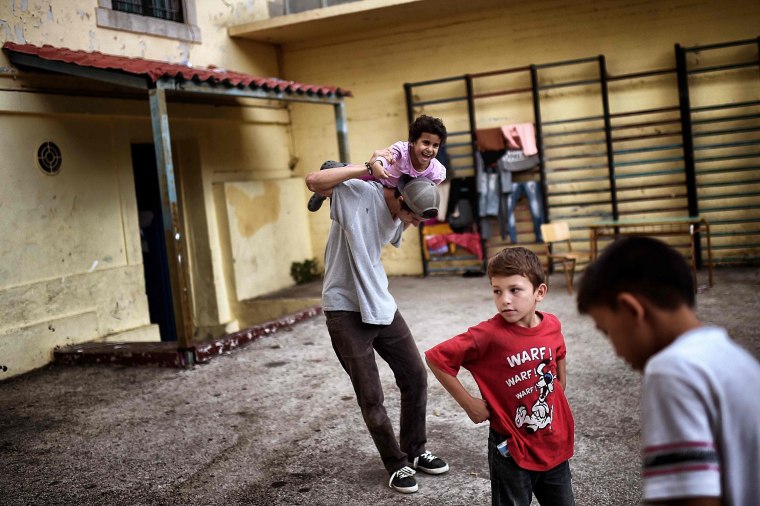Image: Children play at the yard of an abandoned school used by volunteers for hosting families of refugeees