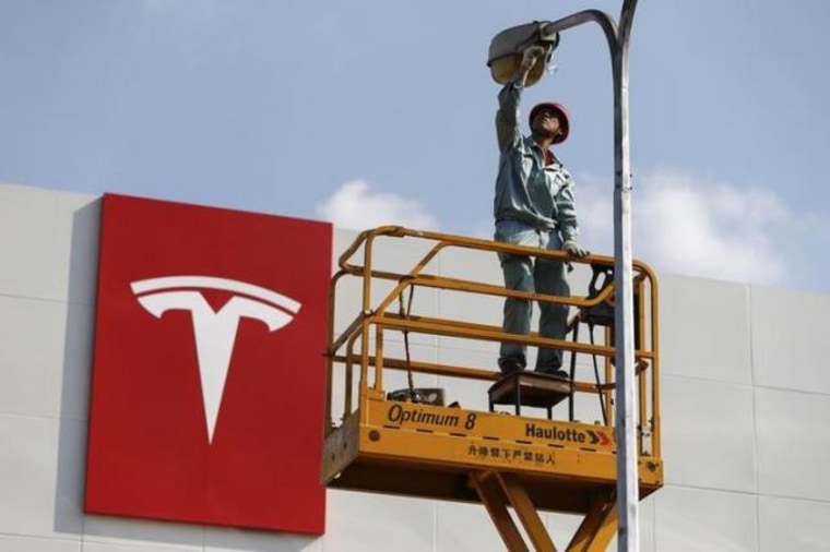 A labourer repairs street lamp next to logo of Tesla Motors in front of new showroom of the company in Shanghai