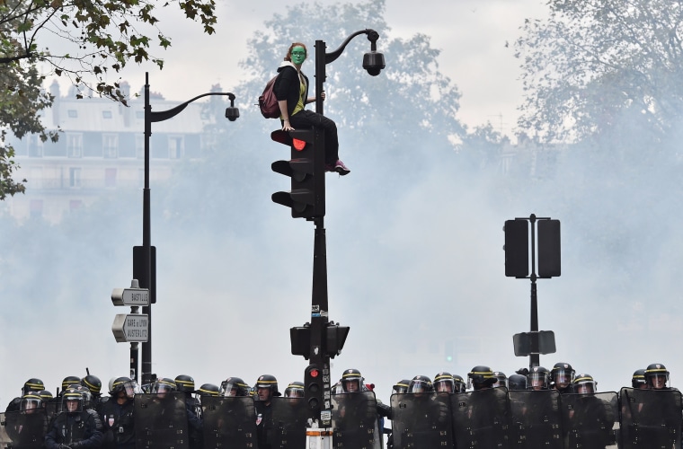 Image: A demonstrator in green face paint sits on a traffic light as French riot police secure the area during a protest against controversial labor reforms