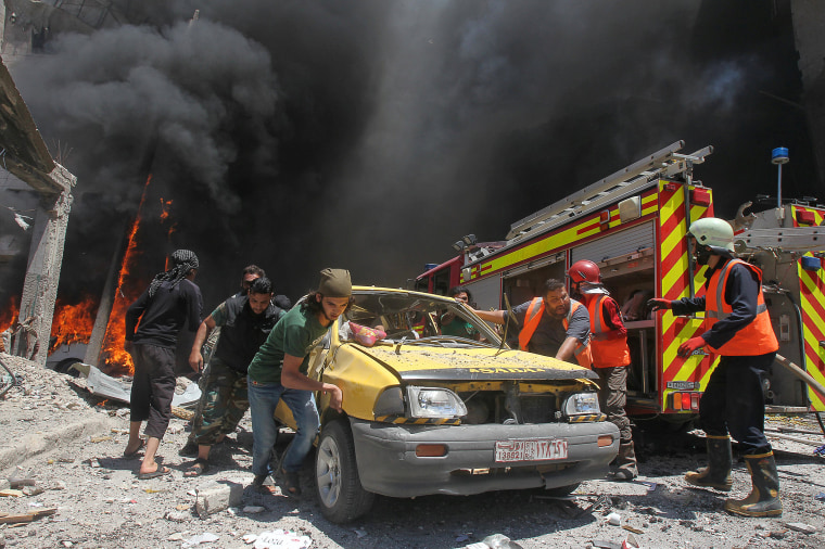 Image: Civil defence members and rescuers push a car at a site hit by air strikes in Idlib city