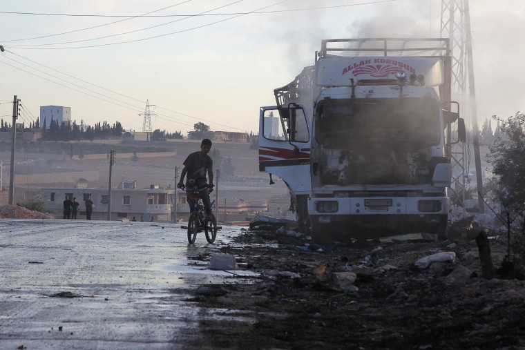 Image: A boy rides a bicycle near a damaged aid truck after an airstrike on the rebel held Urm al-Kubra town
