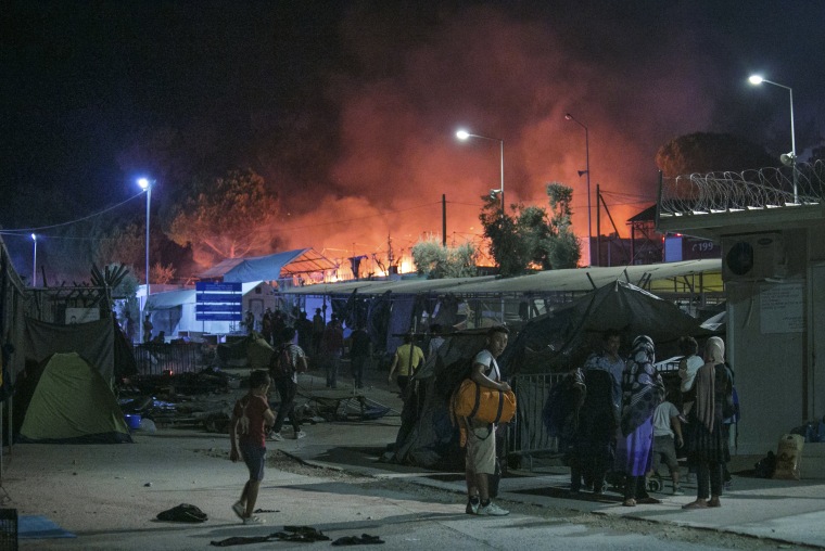 Image: Migrants hold their belonging as a large fire burns inside the Moria refugee camp