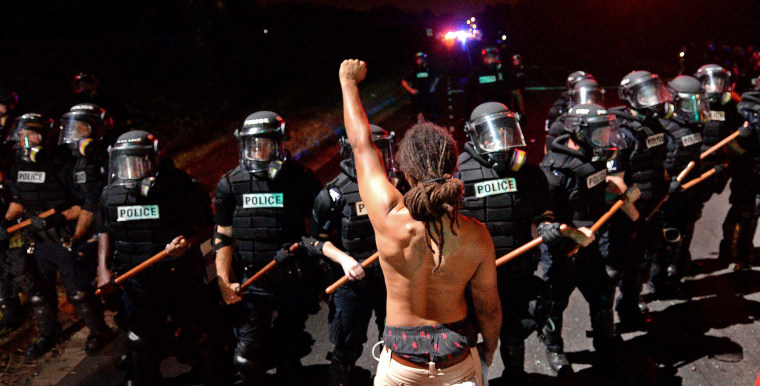 Image: A protester stands with his arm extended and fist clenched in front of a line of police officers in Charlotte