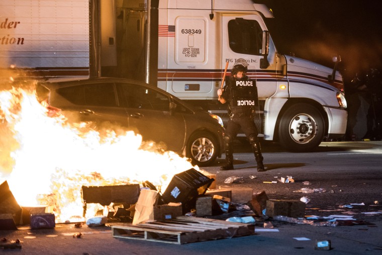 Image: A police officer stands guard near a fire on I-85 during protests