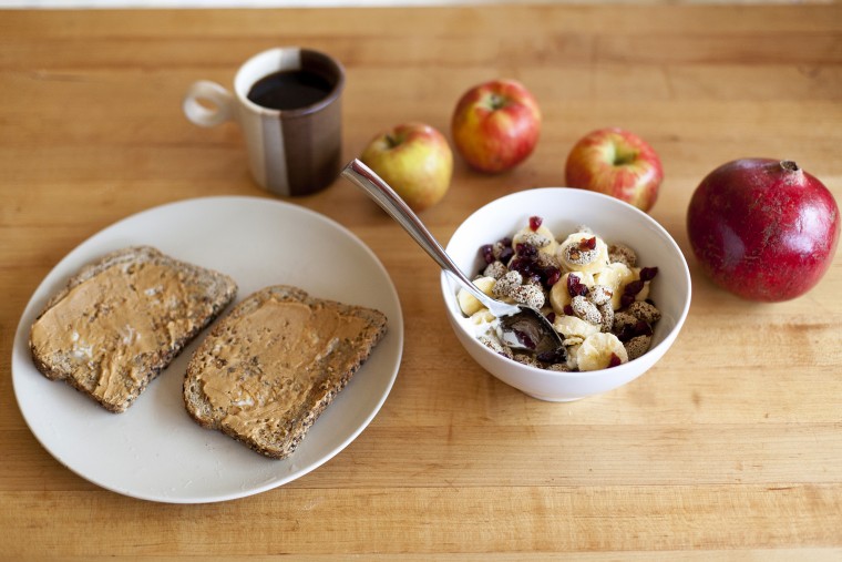 A top down view of a healthy breakfast bowl of cranberries, almonds, Greek yogurt and bananas, also apples, toast with peanut butter and a cup of coffee.
