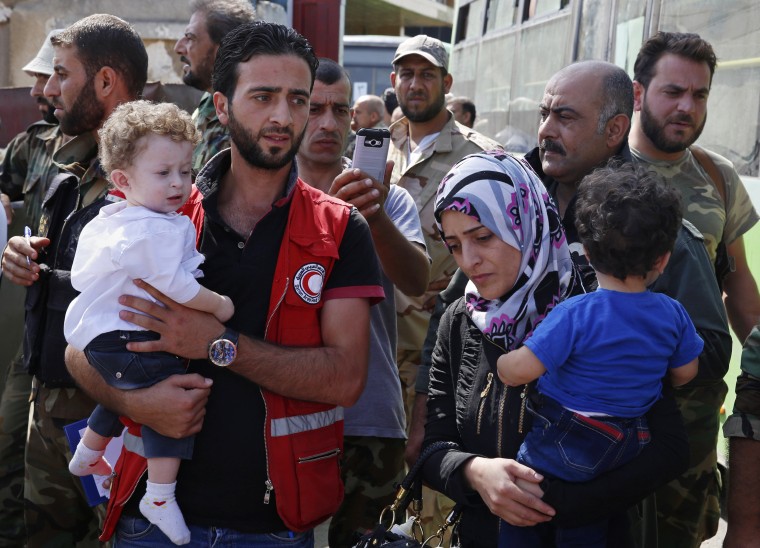 Image: Staffers of the Syrian Arab Red Crescent assist families of gunmen as they leave from Al-Waer